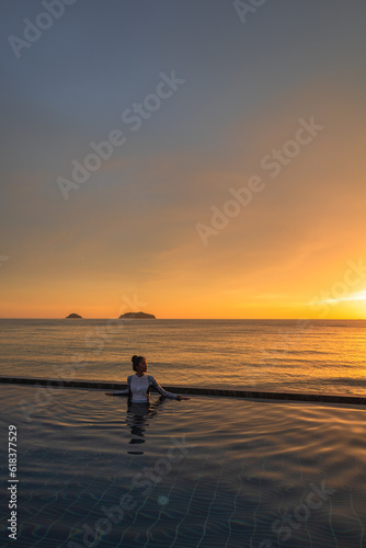 Woman relaxing at the edge of infinity swimming pool at sunset