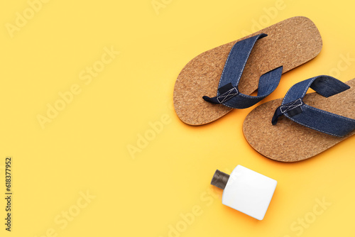 Flip-flops with bottle of sunscreen cream on orange background