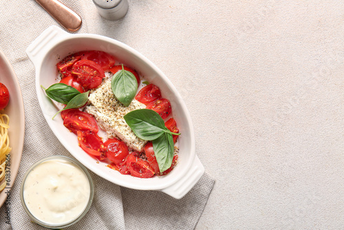 Baking dish with tasty tomatoes and feta cheese on light background