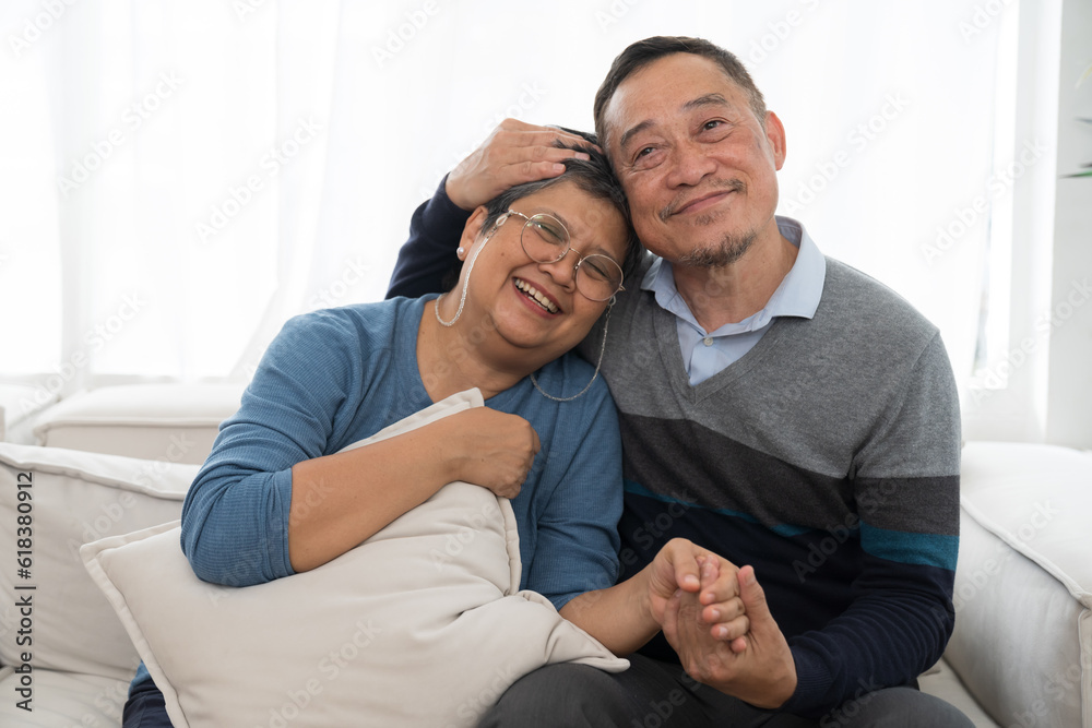 Happy smiling Asian elderly couple hugging together at home. Asian senior man embracing elderly woman on sofa in living room at home. Retirement, health care, relax and spending time concept Happy smiling Asian elderly couple hugging together at home. Asian senior man embracing elderly woman on sofa in living room at home. Retirement, health care, relax and spending time concept