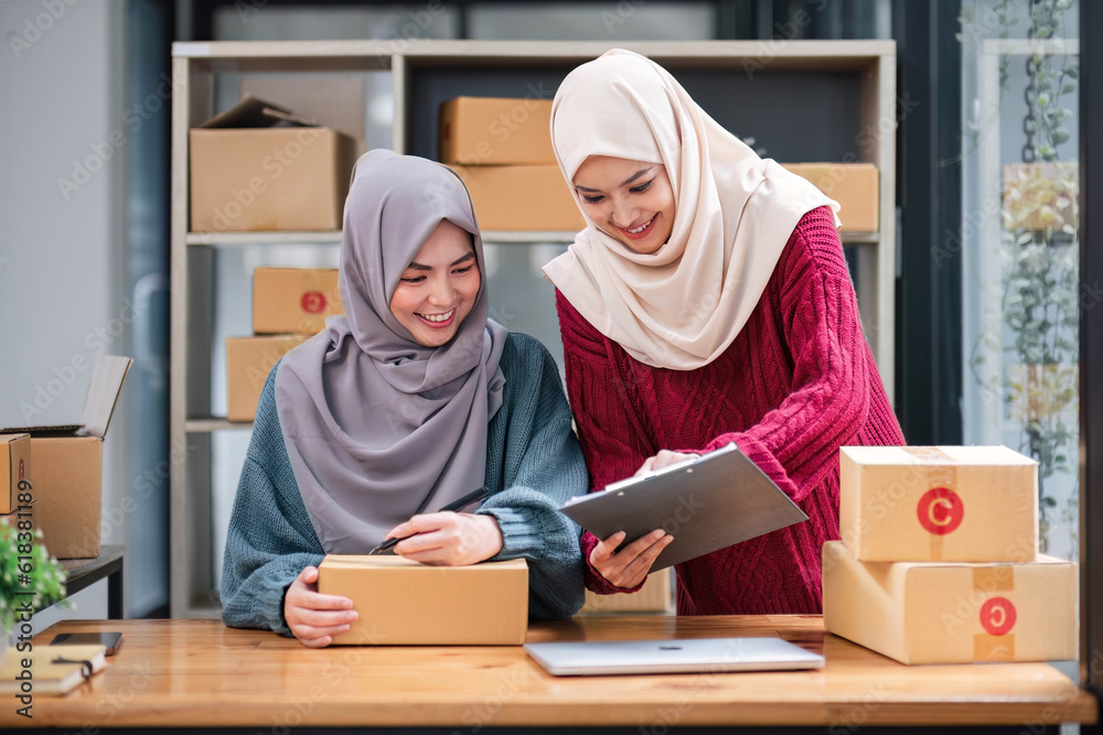 A happy young Asian Muslim female online seller working with her employee in the office. SME business, online shop owner A happy young Asian Muslim female online seller working with her employee in the office. SME business, online shop owner