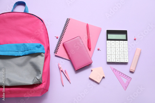 Pink school backpack with notebooks, calculator and pen on lilac background