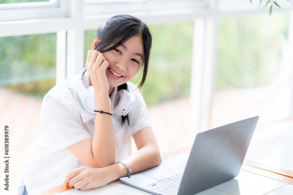 Happy of cute smiles Asian of attractive young Cute girl little wearing headphones using laptop computer working from at the cafe.Online education, elearning concept.