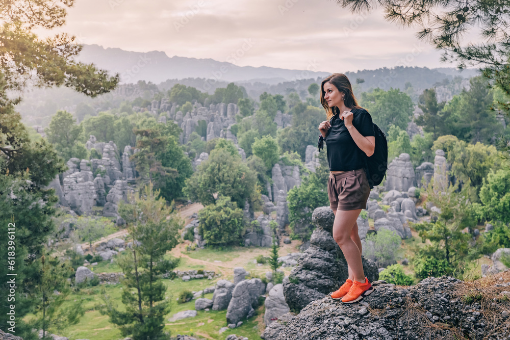Obraz premium Happy traveler girl standing on top of the rock cliff with view of stone remnants in Altinkaya, Turkiye. Tourist attractions and destinations