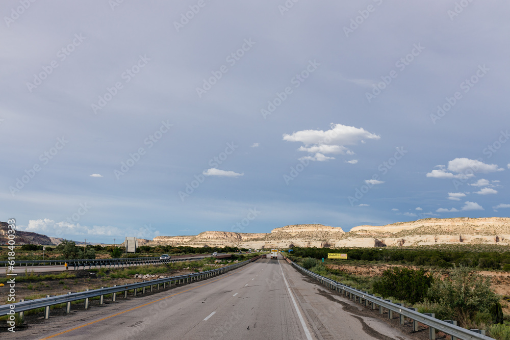 Beautiful summer landscape with highway among rocky mountains and dark blue sky with fluffy clouds on a summer day at sunset. American Roadscape with red canyons in New Mexico near Albuquerque, USA