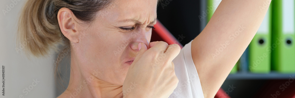 Young woman sniffing armpits and covering nose