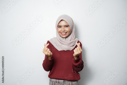 Beautiful smiling Asian woman in red sweater showing Korean heart with two fingers crossed, express joy and positivity isolated over white background © rizkiwanggono