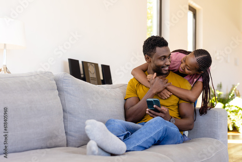 Happy african american couple embracing and using smartphone in living room