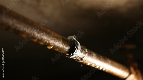 On a rusty metal water pipe in the basement, there is a clamp with a gasket. An old water pipe is leaking.Endless looping video.