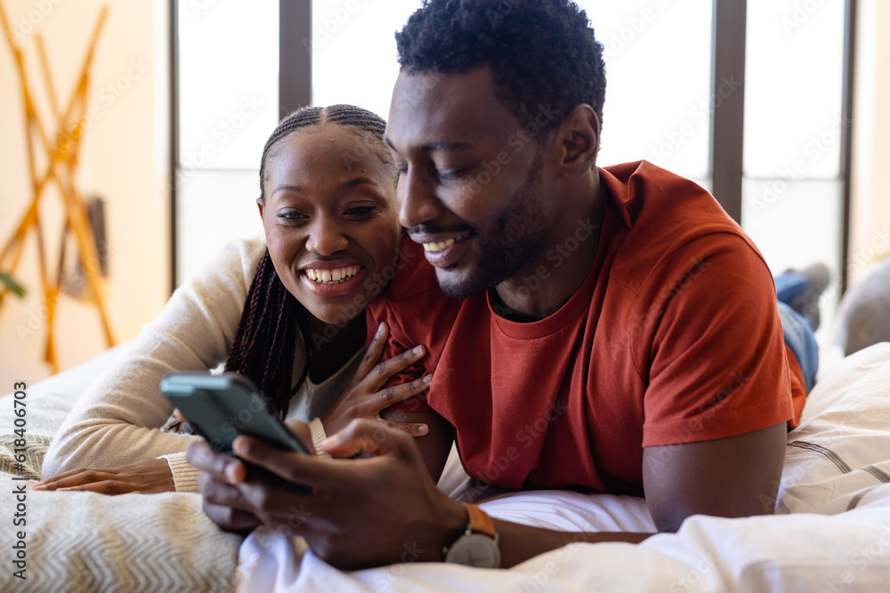 Happy african american couple using smartphone lying on bed in bedroom Happy african american couple using smartphone lying on bed in bedroom