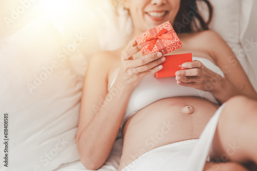 Concept Motherhood and Pregnant, Emotional loving moment in pregnancy timehappy expectant mother during pregnancy. Smiling woman naked belly on bed in bedroom. On Hand holding gift for future baby. photo