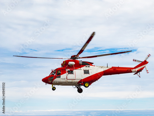 Rescue service on helicopter on volcano above the clouds. Blue sky line on horizon dark volcanic rocks on ground white and red helicopter. Vacation tour on helicopter