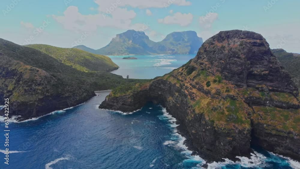 Aerial of the foamy blue sea surrounded by the big rocky cliffs on a sunny day