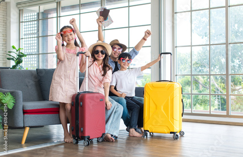 Asian cheerful happy family mom dad son and daughter wearing sunglasses and hat with two trolley luggages raising hands smiling celebrating holiday together ready for traveling vacation road trip photo