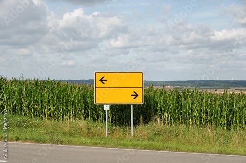 Yellow direction street sign pointing down a winding country road