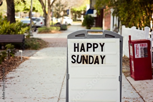 Street sign with the words 'Happy Sunday' written on it, placed on the side of the road