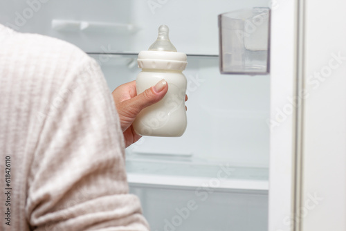 Fotografija Bottle feeding full of milk in cropped woman hand putting it into refrigerator f