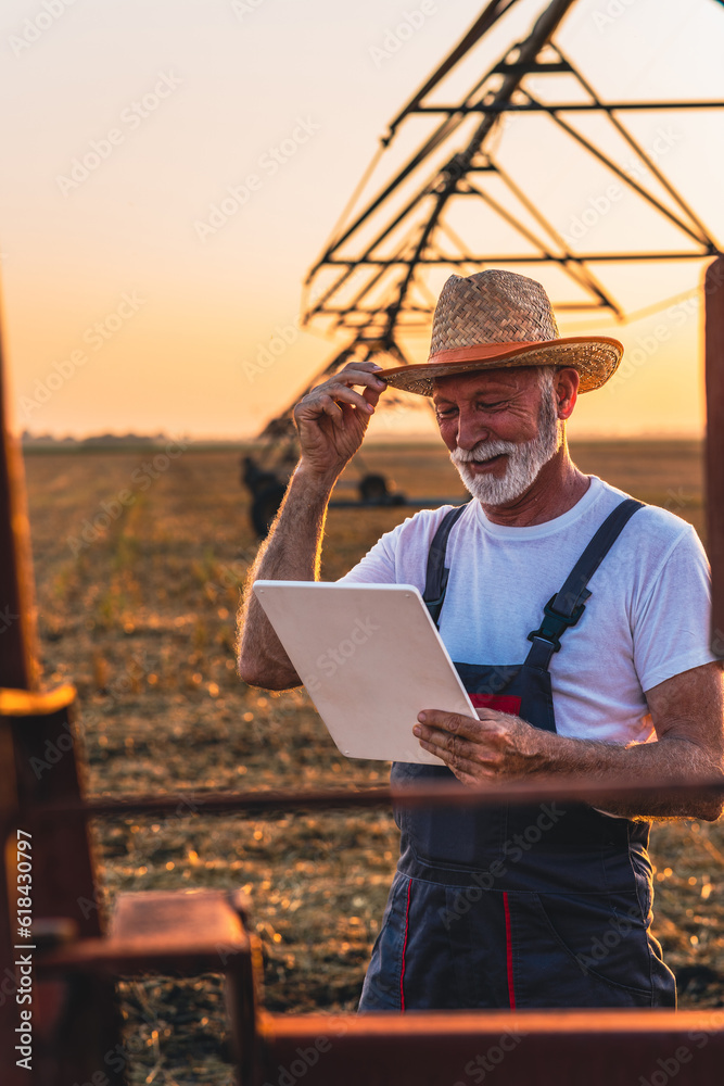 Older farmer holding tablet in his hands and adjusts irrigation system on field at sunset. Older farmer holding tablet in his hands and adjusts irrigation system on field at sunset.