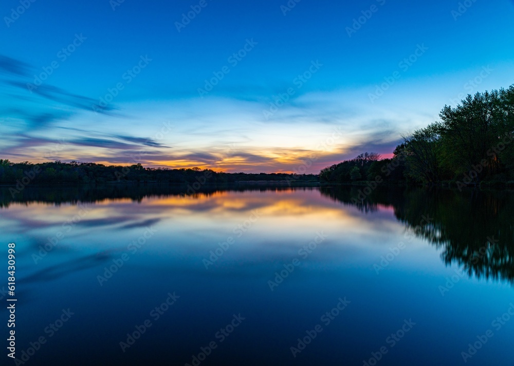 Idyllic image of a peaceful lake surrounded by lush trees, with a dramatic sunset in the background