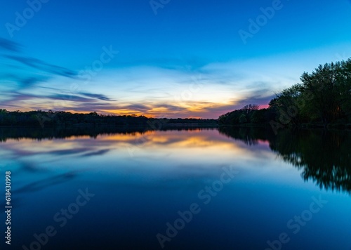 Idyllic image of a peaceful lake surrounded by lush trees  with a dramatic sunset in the background