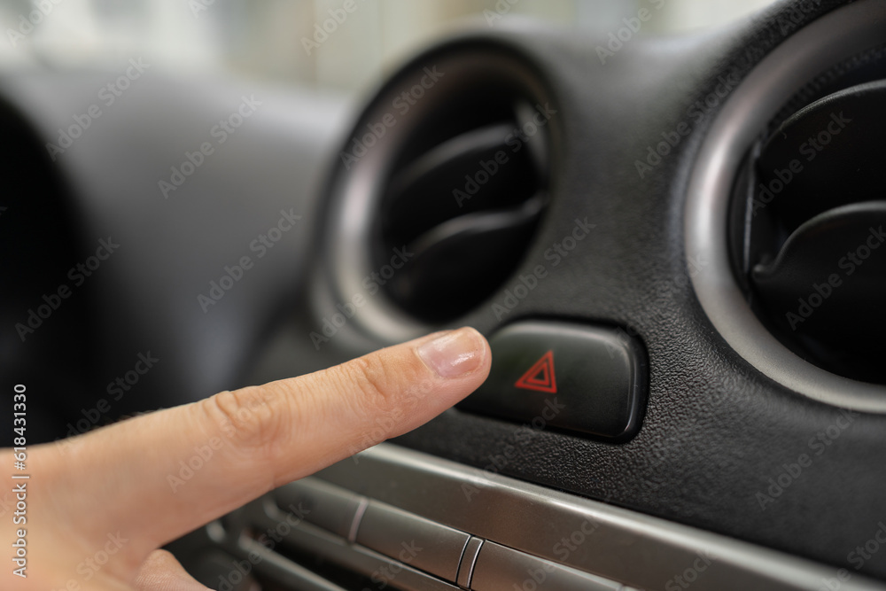 Female finger hitting emergency light stop button in the car, woman pressing red triangle car hazard warning button.