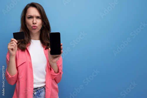 brunette young woman in pink shirt and jeans with phone and money card mockup on studio isolated background