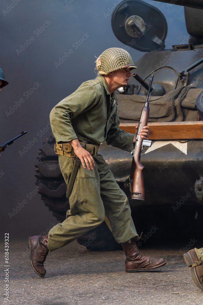 Historical reconstruction. An American infantry soldier from the World War II  prepare to attack hidden behind a tank. 