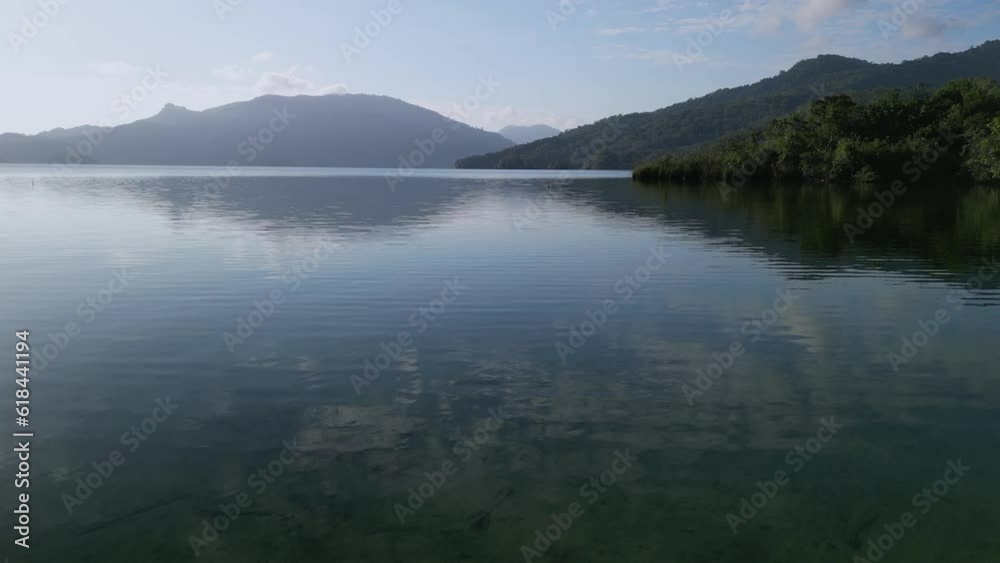 Aerial of a lake surrounded by green forests and mountains on a sunny day Aerial of a lake surrounded by green forests and mountains on a sunny day