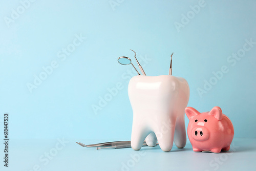 Pink piggy bank and tooth model with medical instruments on blue background. Investing in dental health care.