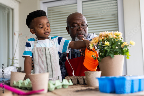 Happy african american grandfather and grandson watering flowers on terrace