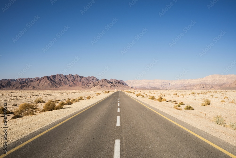 Single-lane desert highway stretching out into a clear blue sky