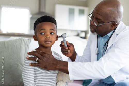 Senior african american male doctor checking ear of boy patient with otoscope photo