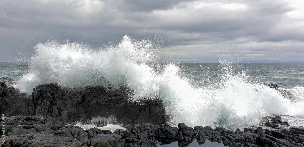 Waves crashing onto the rocky shoreline beneath a cloudy sky on the Isle of Skye.