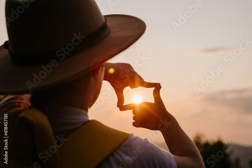 New year planning and vision concept. Close up of child hands making frame gesture on background beautiful sunset. Preteen girl in hat capturing amazing sunrise in mountains at summertime