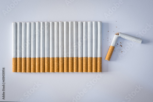 Cigarettes lined up on a white colored plane, the last cigarette is broken, stop smoking concept.