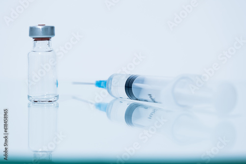 An ampoule and a syringe are placed on a reflective plane, white background, concept of science, research.