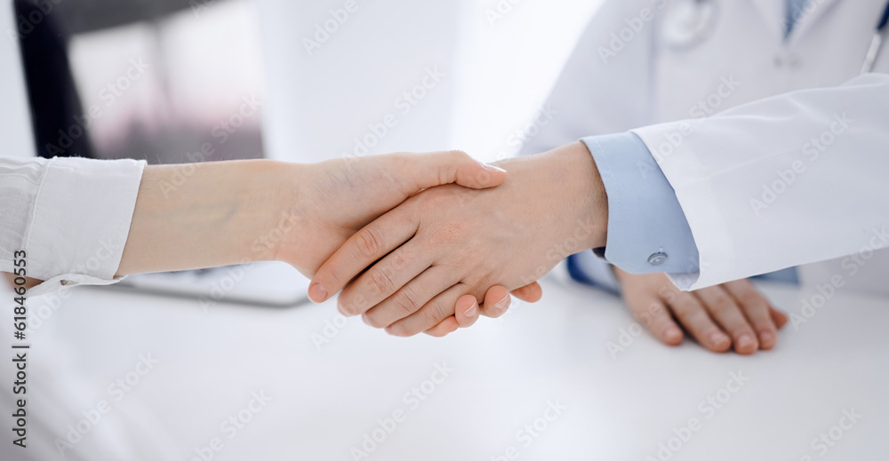 Doctor and patient shaking hands while sitting opposite of each other at the table in clinic, just hands close up. Medicine concept Doctor and patient shaking hands while sitting opposite of each other at the table in clinic, just hands close up. Medicine concept