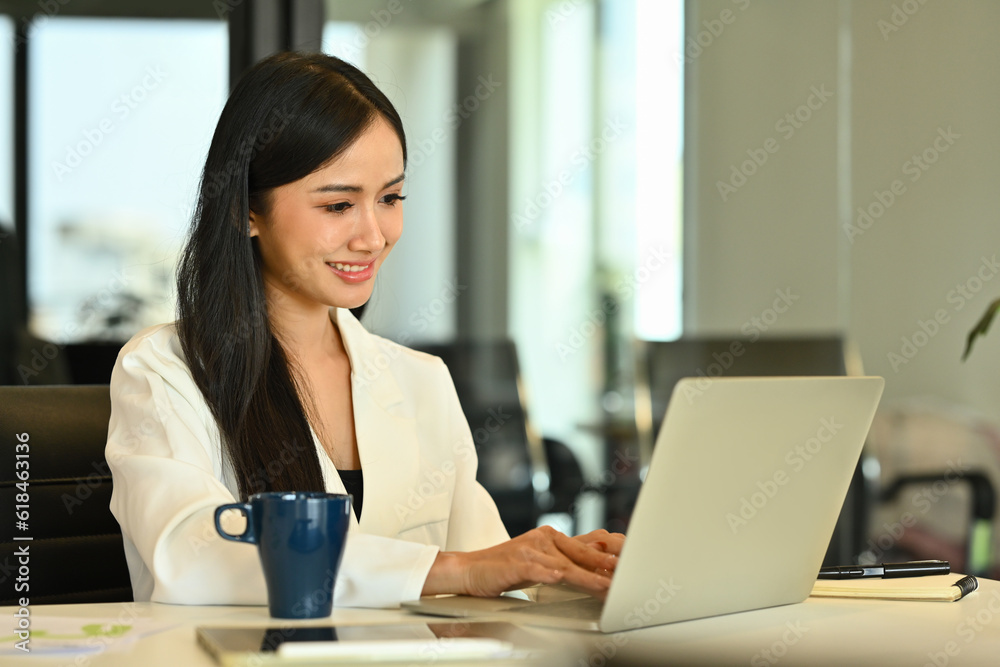 Satisfied businesswoman looking at laptop, analyzing financial data and planning marketing strategy at workplace Satisfied businesswoman looking at laptop, analyzing financial data and planning marketing strategy at workplace