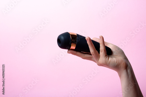 Female hand is holding black vacuum clitoral stimulator on a pink background. Place for text. Sex shop concept. Copy space photo