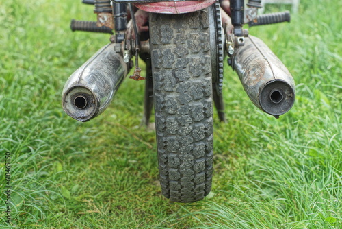 Fototapeta Naklejka Na Ścianę i Meble -  part of iron rusty dirty old chrome exhaust pipes with old motorcycle wheel of retro old motorbike on green grass outdoors at daytime