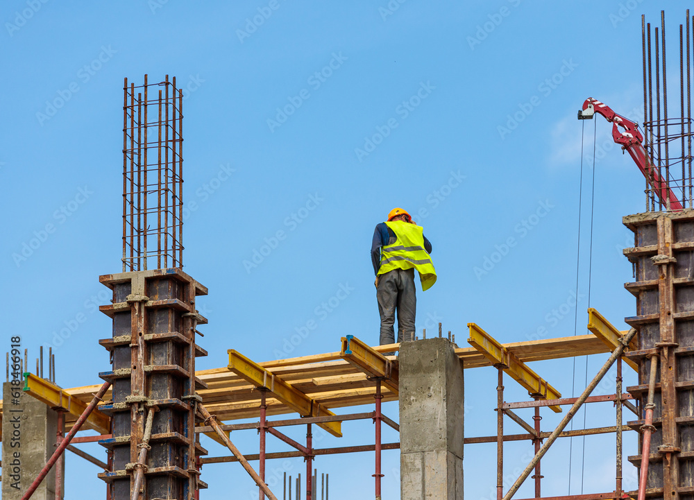 A male construction worker stands on reinforced concrete beams at a height.