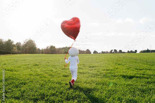 Girl dressed as astronaut walking on meadow holding heart shape balloon