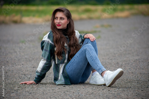 A beautiful young girl in jeans sits on the road
