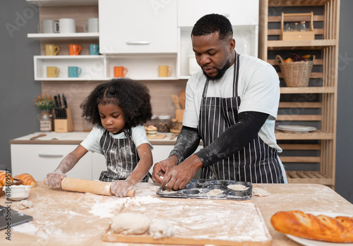 Happy African American kid girl with family cooking break or bakery at kitchen at home 