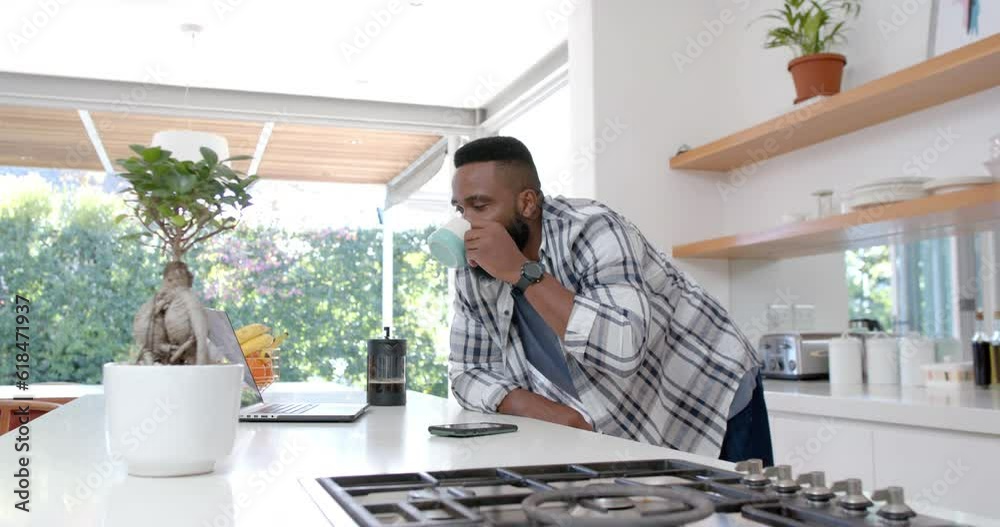 African american man making coffee and using laptop in sunny kitchen, slow motion African american man making coffee and using laptop in sunny kitchen, slow motion