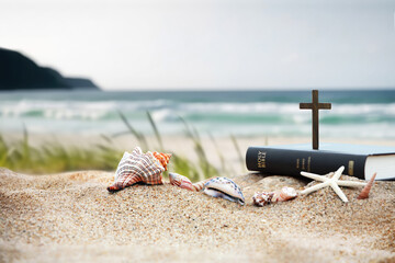 Church summer retreat concept with bible book, cross of Jesus Christ and shells, conch and starfish on sandy beach and sea with waves Summer bible school summer camp background
