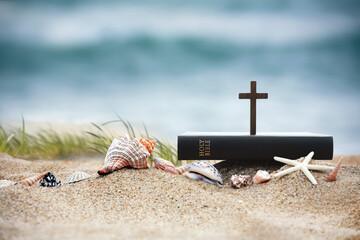 Church summer retreat concept with bible book, cross of Jesus Christ and shells, conch and starfish on sandy beach and sea with waves Summer bible school summer camp background
