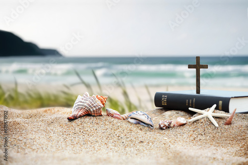 Fototapeta Naklejka Na Ścianę i Meble -  Church summer retreat concept with bible book, cross of Jesus Christ and shells, conch and starfish on sandy beach and sea with waves Summer bible school summer camp background
