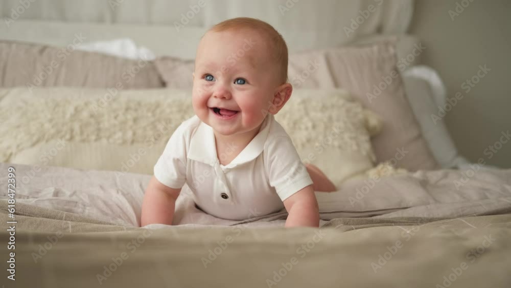 Happy baby. Cute little newborn girl with smiling face crawling on bed in bedroom. Infant baby resting playing lying down on blanket at home. Motherhood happy child childcare concept Happy baby. Cute little newborn girl with smiling face crawling on bed in bedroom. Infant baby resting playing lying down on blanket at home. Motherhood happy child childcare concept