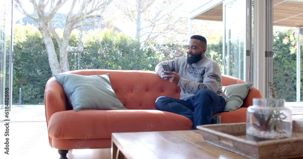 African american man using smartphone in sunny living room, slow motion African american man using smartphone in sunny living room, slow motion